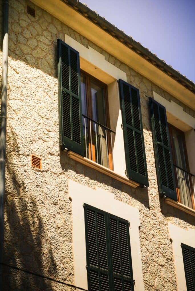 Sunlit facade of a traditional Mediterranean stone house with shutters in Balearic Islands, Spain.