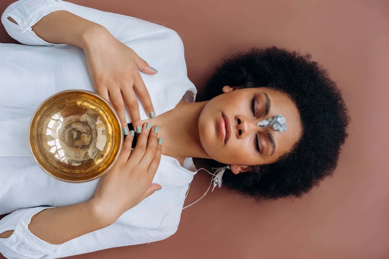 A woman meditates with a Tibetan singing bowl and crystals, promoting wellness and spiritual healing.
