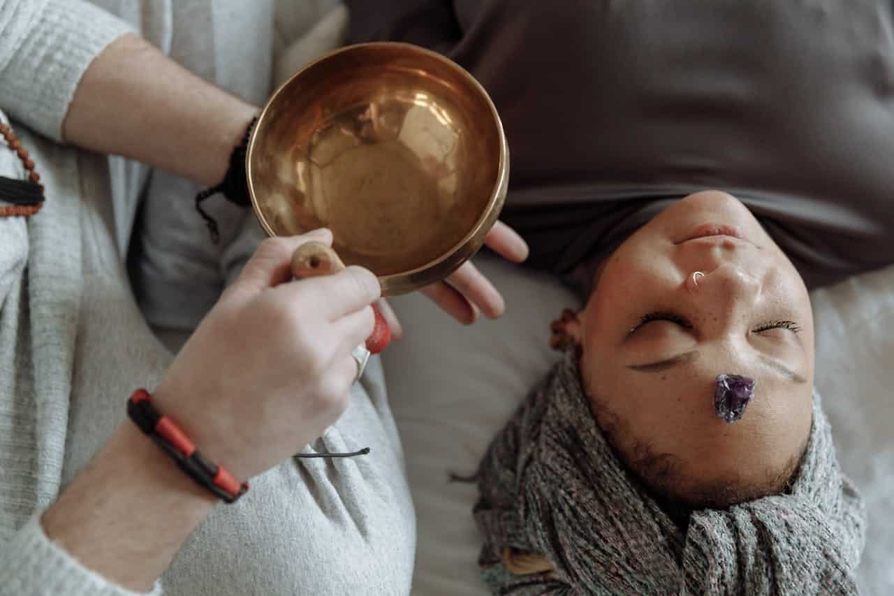 Woman receiving healing therapy with a Tibetan singing bowl placed during meditation.