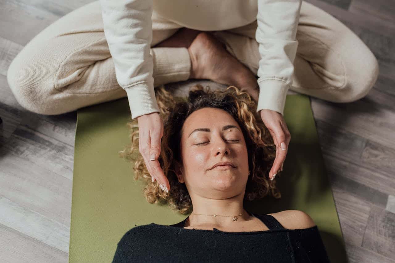 A woman receiving relaxing Reiki therapy on a yoga mat indoors.